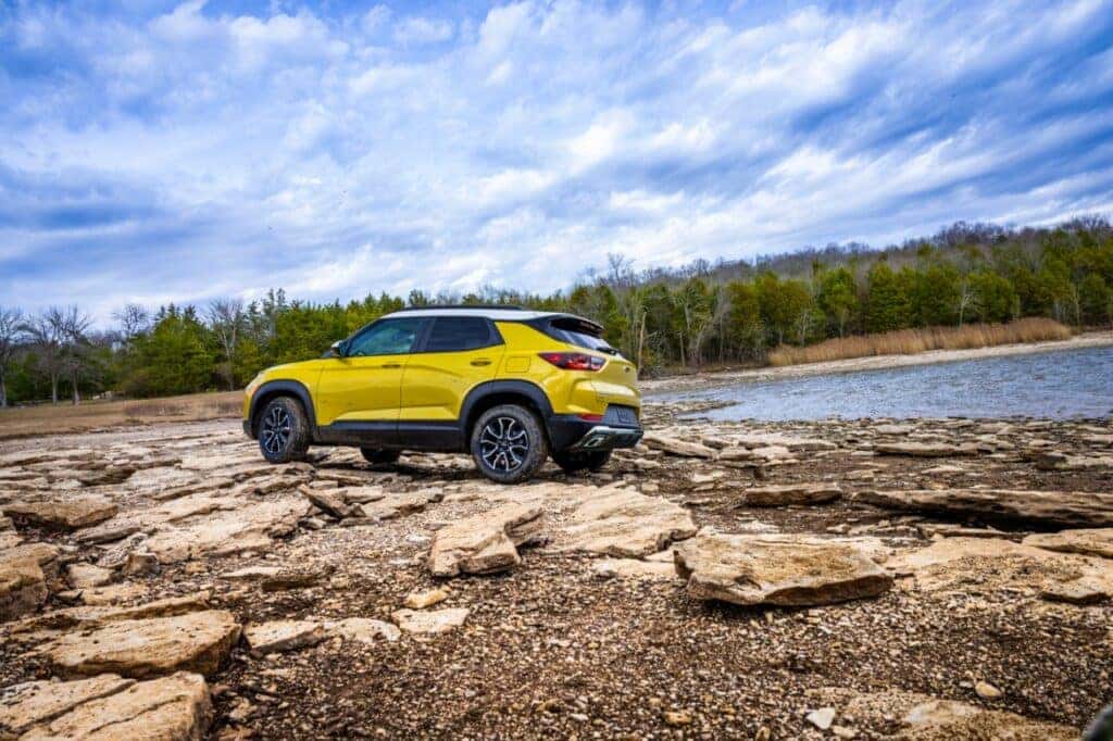 Rear 7/8 view of 2024 Chevrolet Trailblazer ACTIV in Copper Harbor Metallic parked by a lake at sunset. Preproduction model shown. Actual production model may vary. Available in fall 2023.