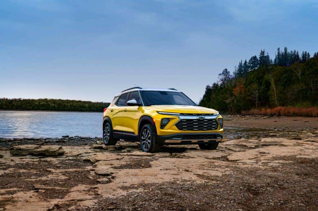 Front 3/4 view of 2024 Chevrolet Trailblazer ACTIV in Copper Harbor Metallic parked on a rock bank in front of a lake. Preproduction model shown. Actual production model may vary. Available in fall 2023.