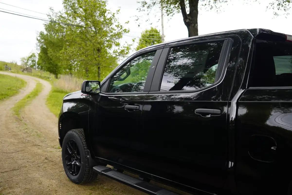 Side view of a black Chevrolet Silverado crew cab truck with black wheels parked next to a winding dirt road