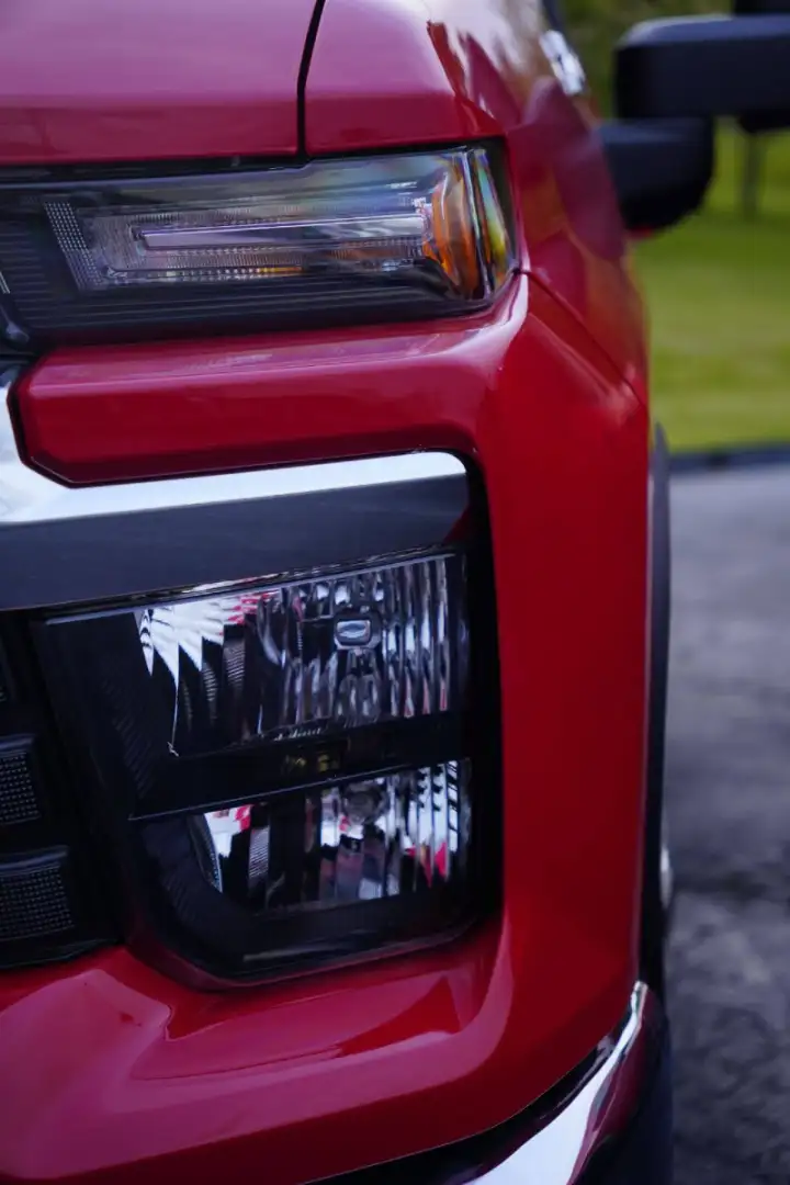 Close-up front view of a red Chevrolet truck showing the detailed headlight assembly and chrome grille accent