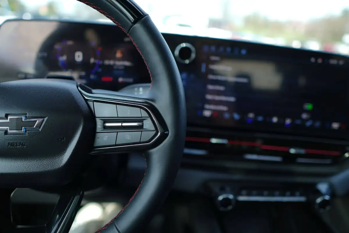 Black leather Chevrolet steering wheel with red stitching showing the digital instrument cluster and infotainment touchscreen in the background.