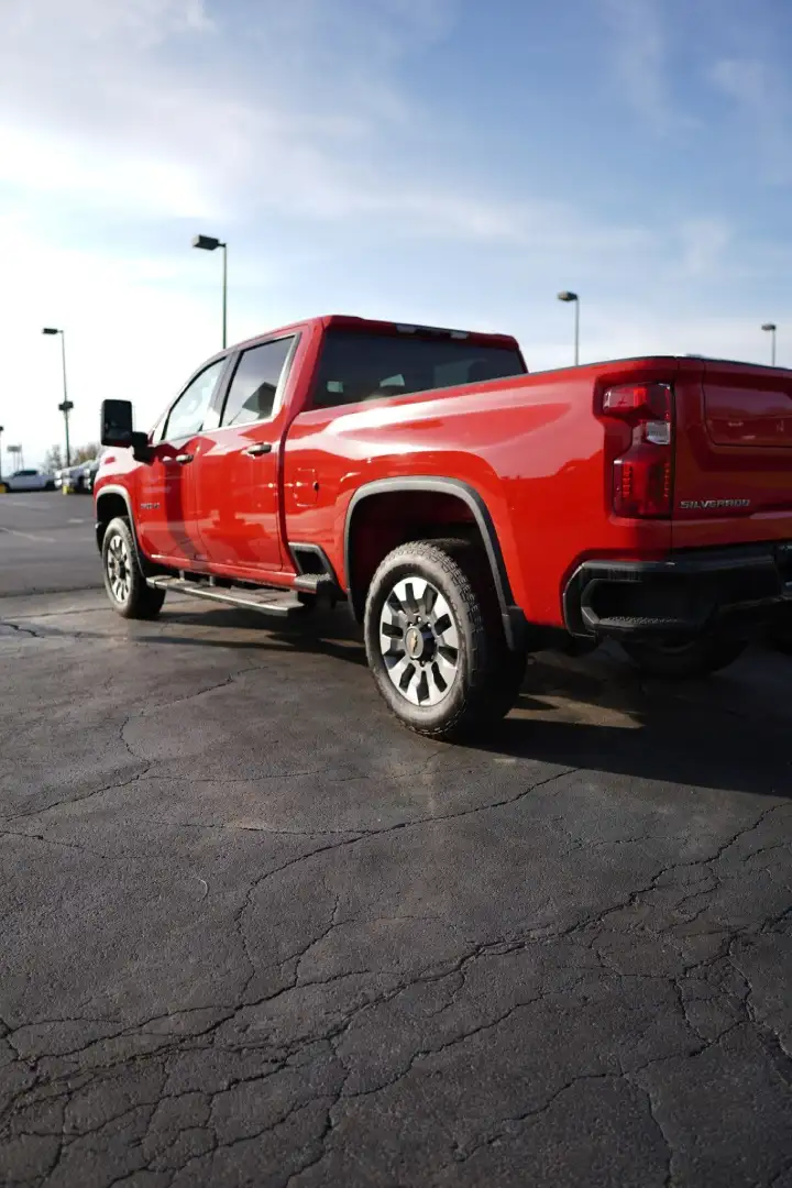Rear three-quarter view of a red Chevrolet Silverado crew cab truck parked on a dealership lot under a blue sky