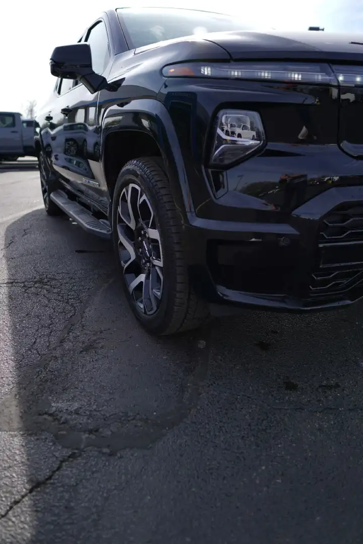 Low-angle front view of a black Chevrolet Silverado EV truck showing the front wheel, futuristic LED headlights, and aggressive front bumper