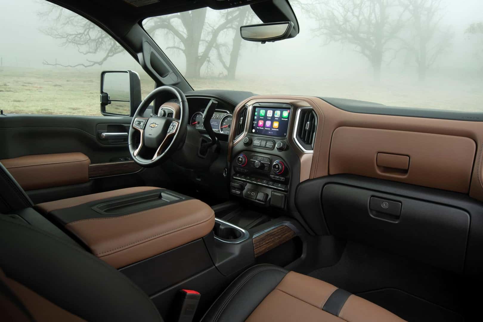 The Cool Interior Of The 2022 Chevrolet Silverado 2500HD. Outside The Windows, There Is Spooky Fog Swarming Around The Branches Of Spindly Trees