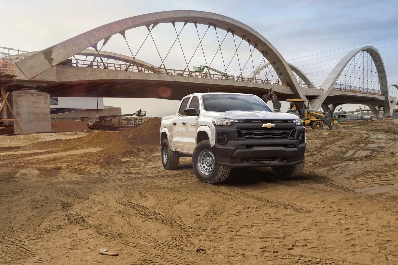 A Hardy 2023 Chevrolet Colorado At A Dusty Construction Site In Front Of A Shining, Metal Bridge