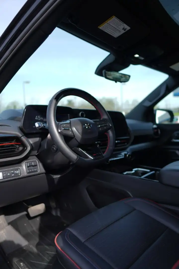 Driver's seat view of a Chevrolet Blazer EV interior featuring red-accented trim and leather steering wheel