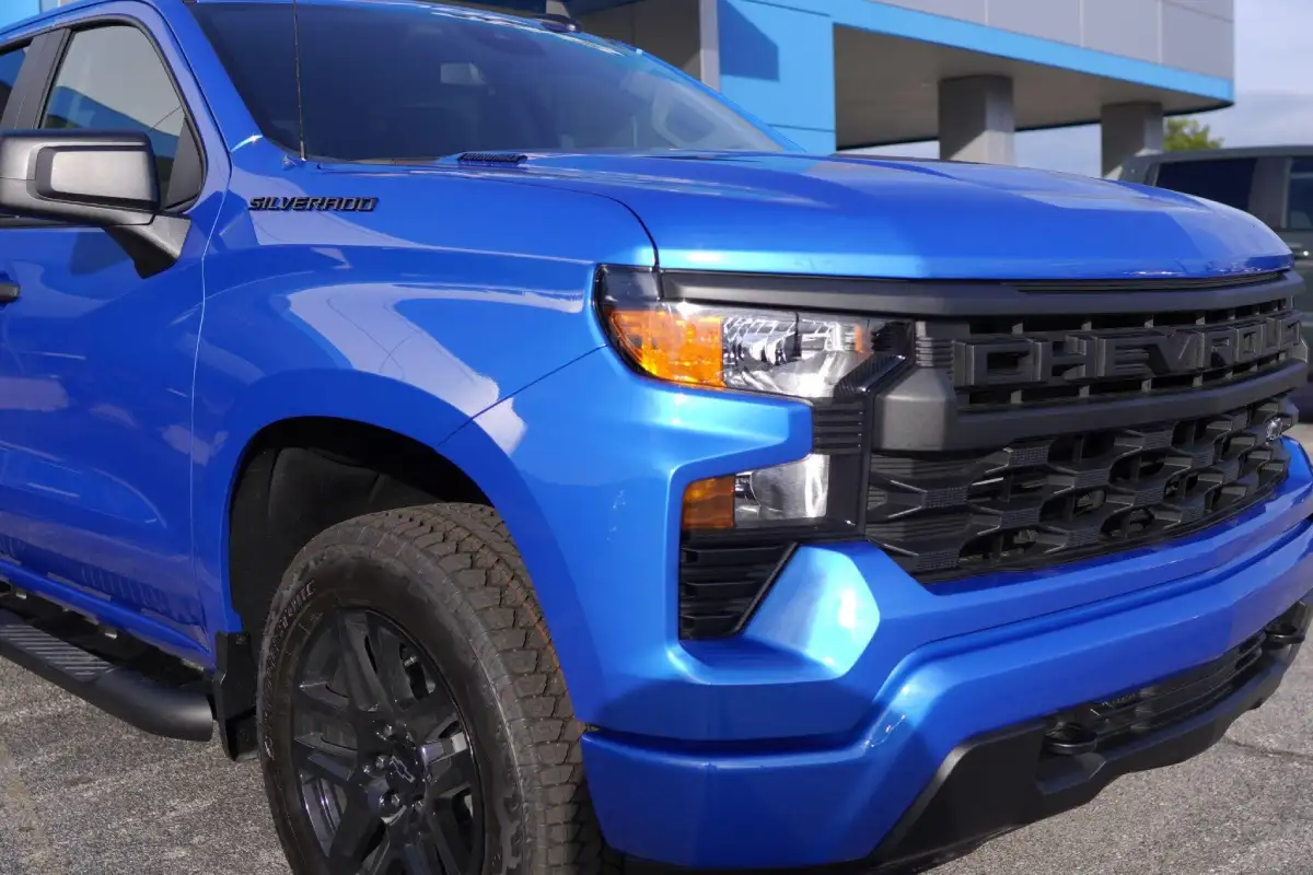Three-quarter front view of a bright blue Chevrolet Silverado Custom Trail Boss pickup truck, showing its blacked-out grille with CHEVROLET lettering, black multi-spoke alloy wheels, and side steps on a dealership lot