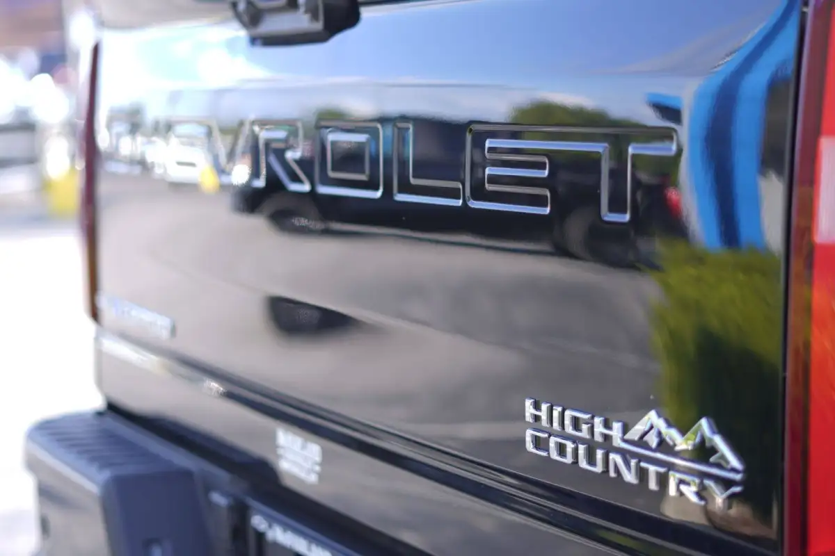 Close-up of the tailgate of a glossy black Chevrolet Silverado, showcasing the embossed "CHEVROLET" lettering and a chrome "High Country" mountain logo badge on the lower right side