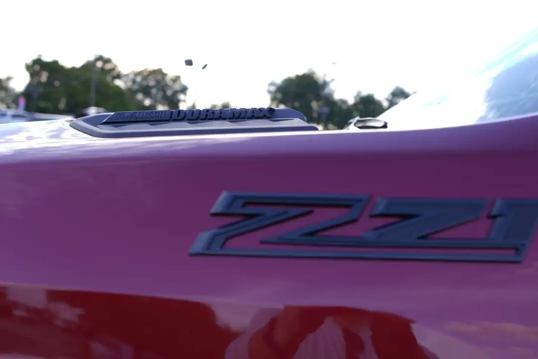 Close-up of a red Chevrolet truck fender showing a dark gray Z71 off-road emblem, with a black Duramax Allison Transmission hood scoop badge visible in the background