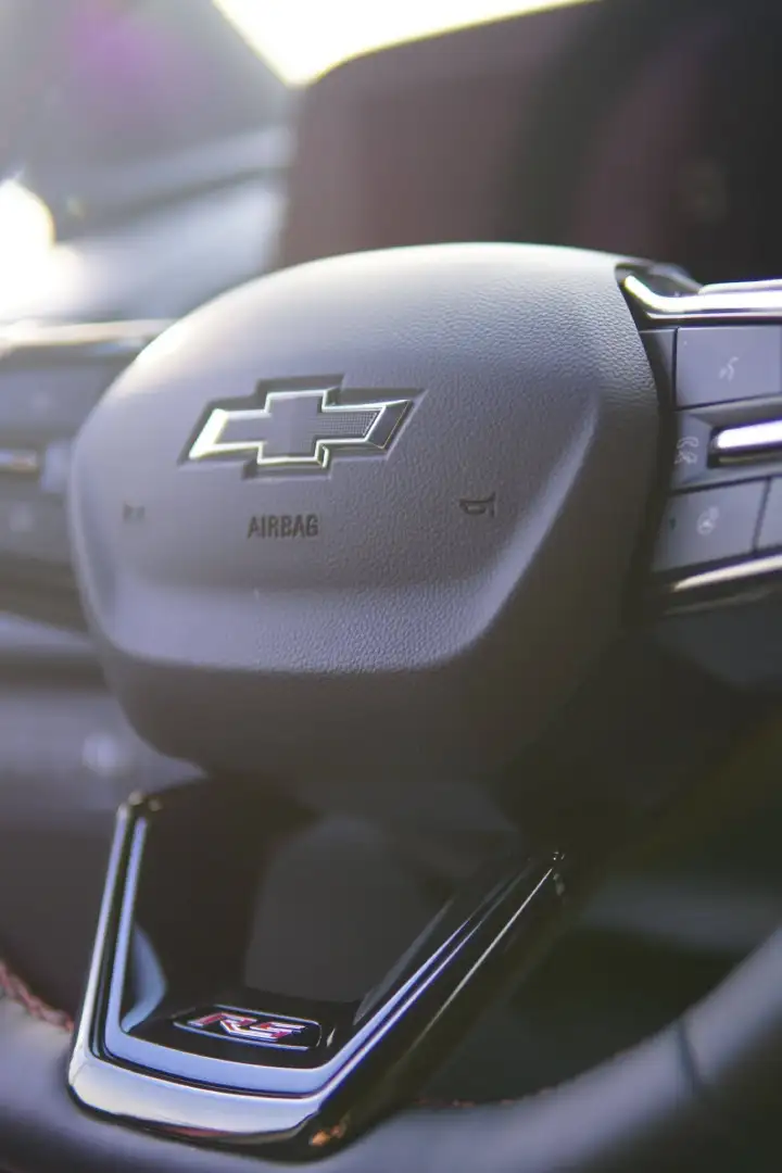 Close-up of a black textured Chevrolet steering wheel hub featuring a prominent bowtie logo, integrated steering wheel controls, and a red and silver RS emblem on the bottom spoke