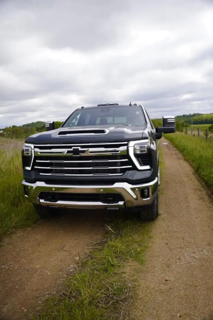 Front view of a dark gray Chevrolet Silverado HD pickup truck parked on a dirt path in a rural field under a cloudy sky
