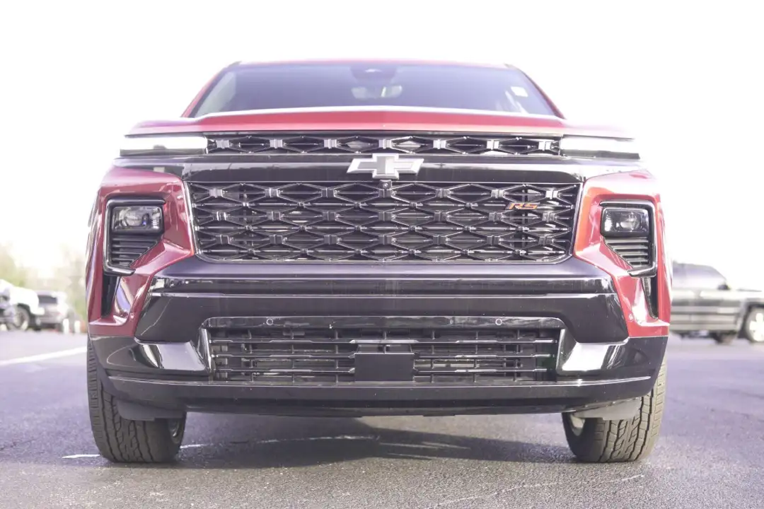 Straight front view of a red Chevrolet Traverse RS SUV on a dealership lot, highlighting its glossy black mesh grille, signature Chevy bowtie badge, and sleek LED headlights