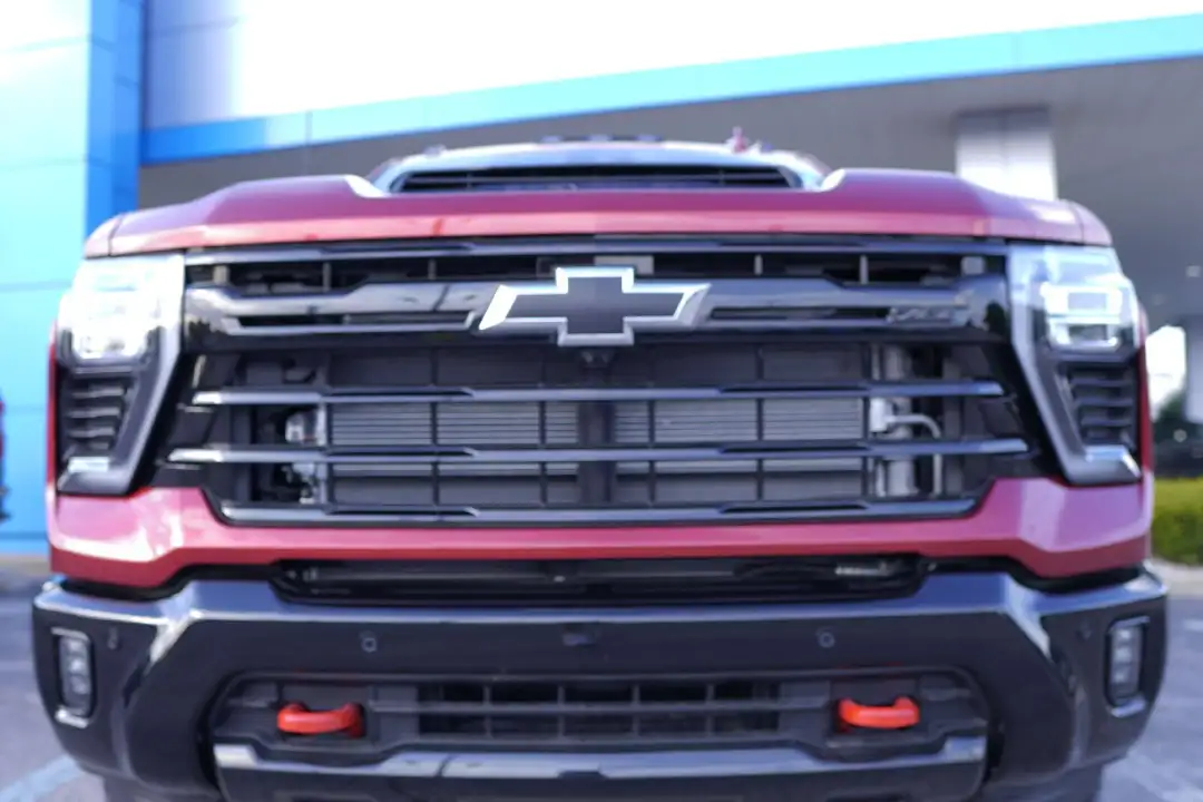 A symmetrical close-up view of the front of a dark red Chevrolet Silverado truck, highlighting its black grille, chrome bowtie emblem, and dual red tow hooks on the lower bumper.