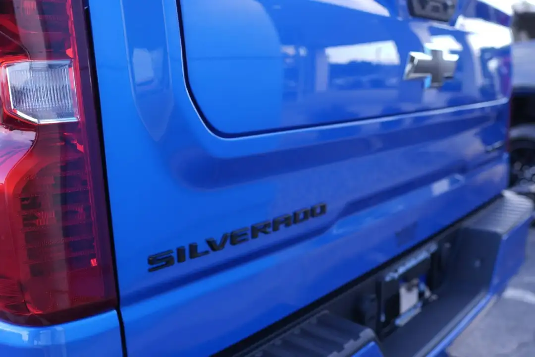 A close-up view of a bright blue Chevrolet pickup truck's tailgate, featuring black embossed "SILVERADO" lettering next to a prominent red and clear vertical taillight assembly.