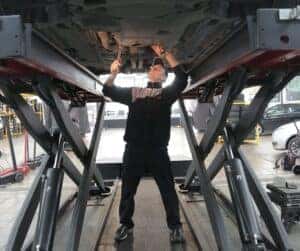 A service technician working on parts underneath a lifted car