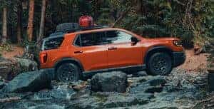 An orange 2026 Honda Passport TrailSport off-roading through rocky terrain in the woods