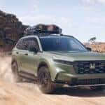 A green 2026 Honda CR-V TrailSport driving with a cargo net through the desert