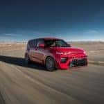 A red Kia Soul driving in the outdoors.