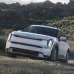 A white 2024 Kia EV9 electric SUV driving up a gravelly hill