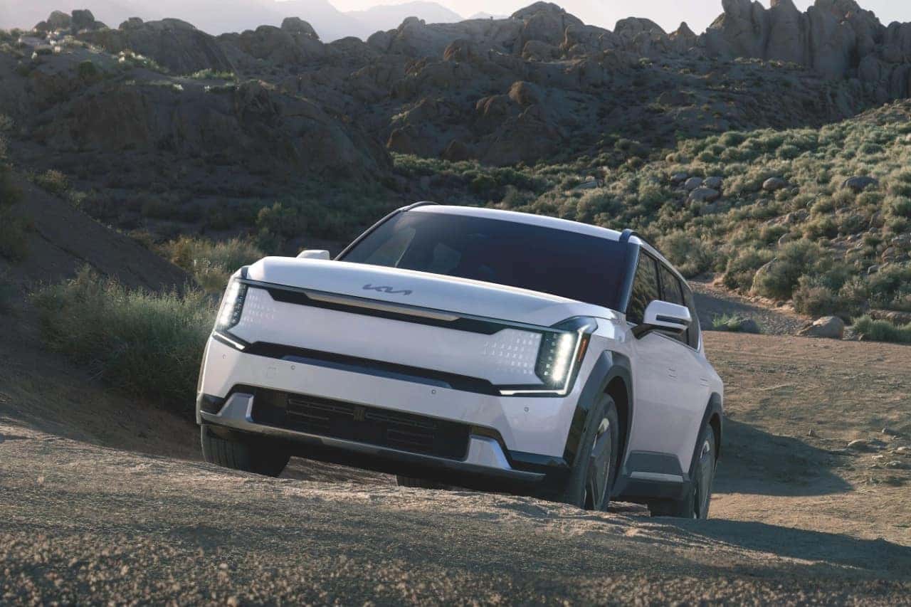 A white 2024 Kia EV9 electric SUV driving up a gravelly hill