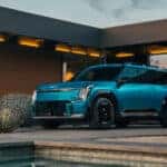 A blue 2025 Kia EV9 parked outside a modern home