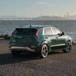 A green 2025 Kia Niro Hybrid parked on the sand facing the water and city skyline