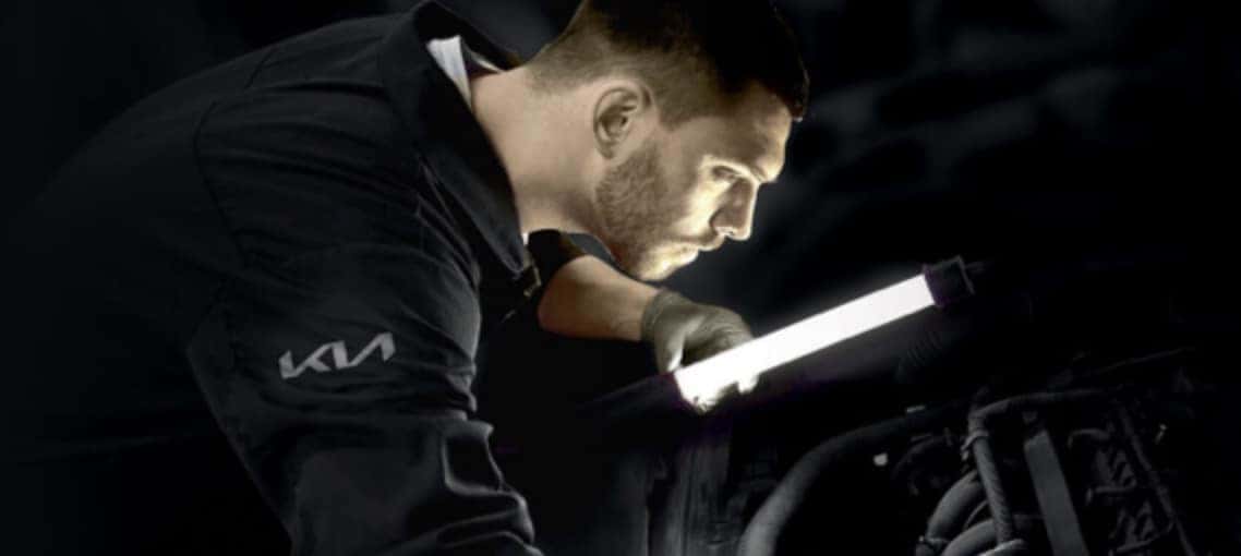 A Kia service technician using a light to look at an engine