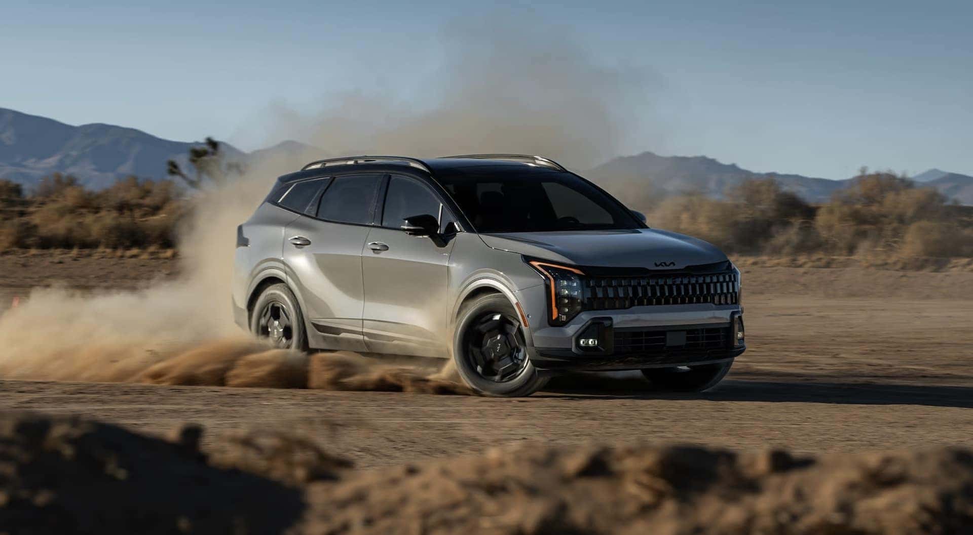 A gray 2026 Kia Sportage driving fast kicking up dirt