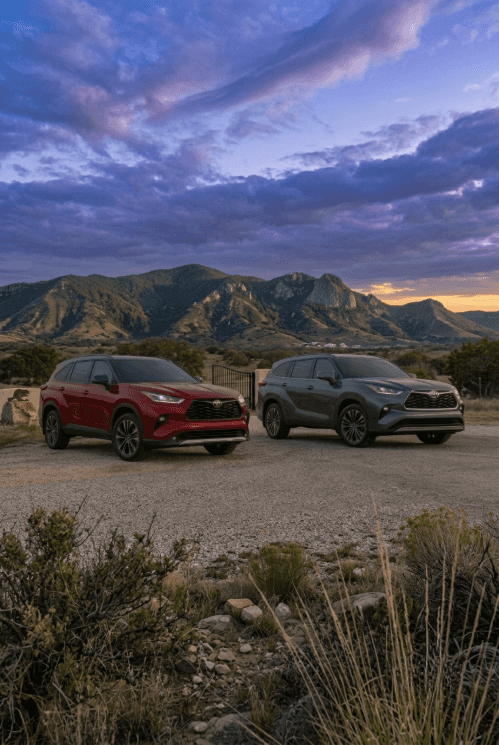 Two Toyota SUVs parked on a gravel path with a scenic mountain landscape under a twilight sky