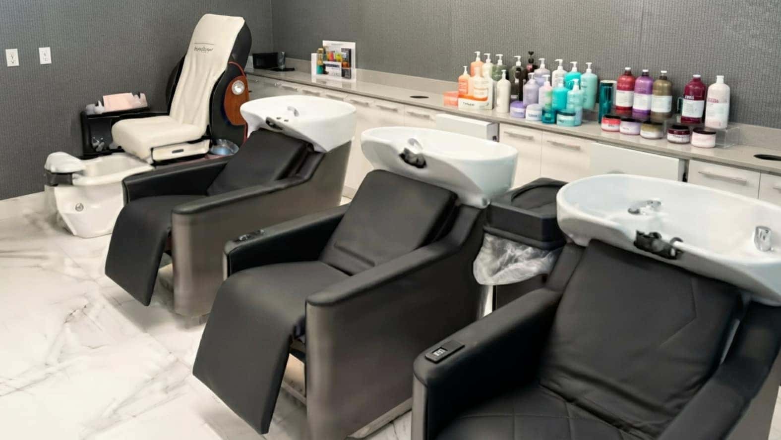 Interior view of Crown and Co Salon showcasing luxury black shampoo backwash chairs with white ceramic basins and marble tile floors