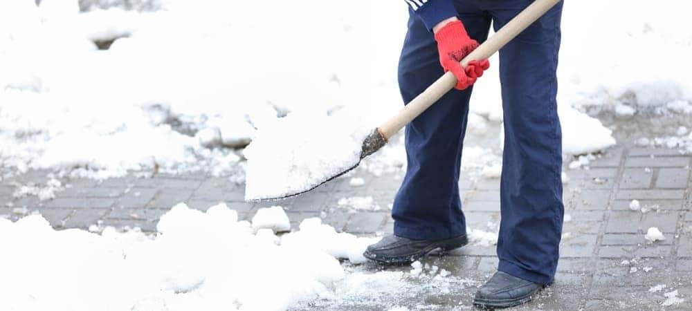 man die sneeuw en ijs van de oprit verwijdert