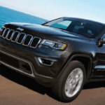 Black 2019 Jeep Grand Cherokee towing boat on highway next to lake