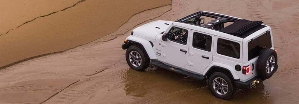 White Jeep Wrangler driving on sand