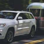 White 2020 Jeep Grand Cherokee towing a silver trailer on wooded road