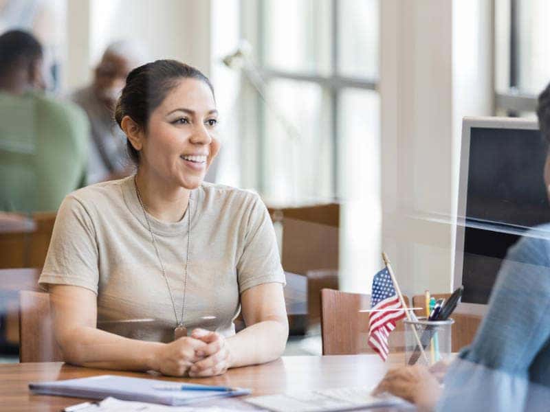 A woman and a man engage in conversation in a modern office setting, surrounded by desks and office equipment.