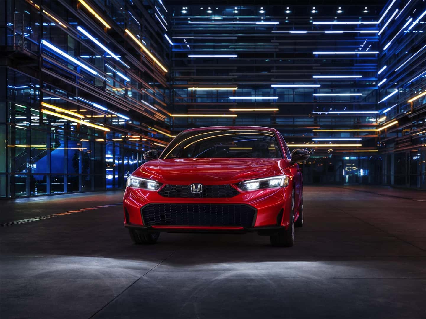 Red Honda Civic Sedan Hybrid in front of neon-lit architecture