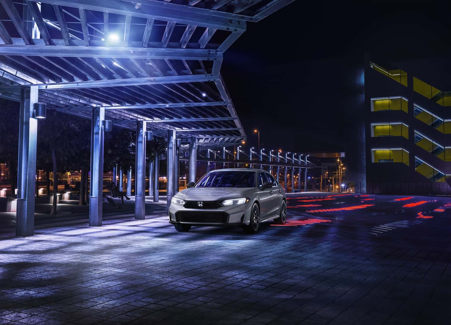 Silver Honda Civic Sedan Sport Hybrid parked beneath illuminated architecture at night