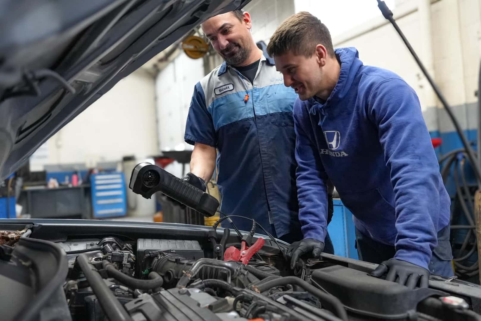 Two Ide Honda technicians working together under the hood of a vehicle