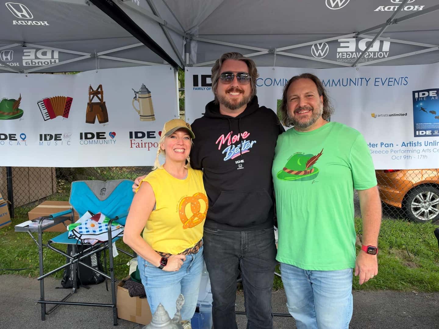 Three people at an Ide community event, with a More Better hoodie in the center