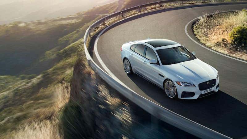 Silver Jaguar XF driving around a curvy road on a mountain
