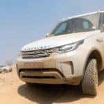 Land Rover Discovery driving on dusty desert hill with another Land Rover in the background