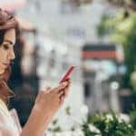 Woman outside on her phone sitting with a cup of coffee