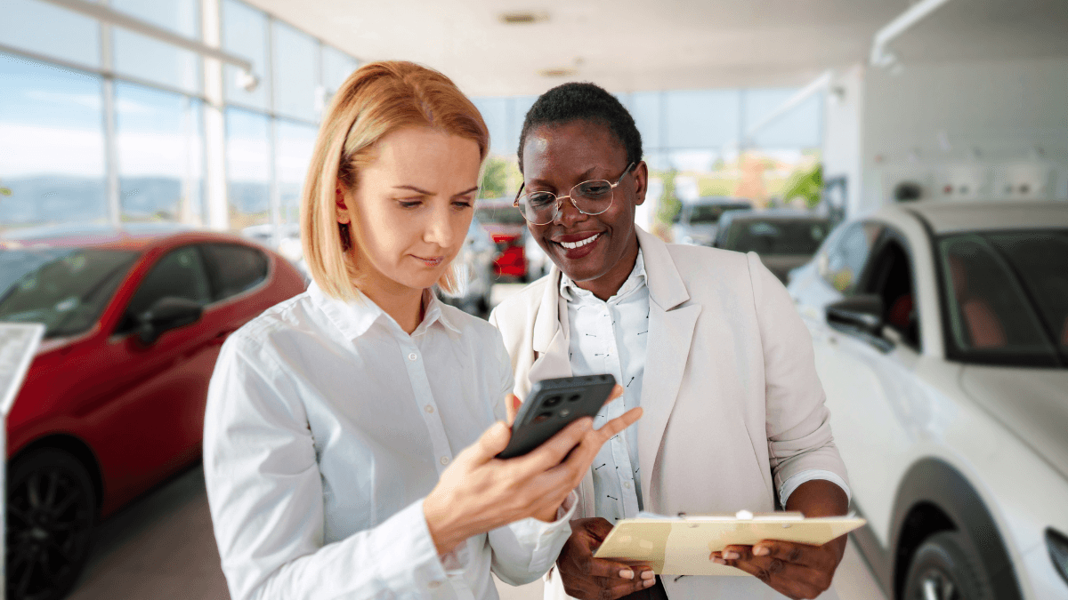 A black saleswoman going over a car sale with a white woman in a dealership.