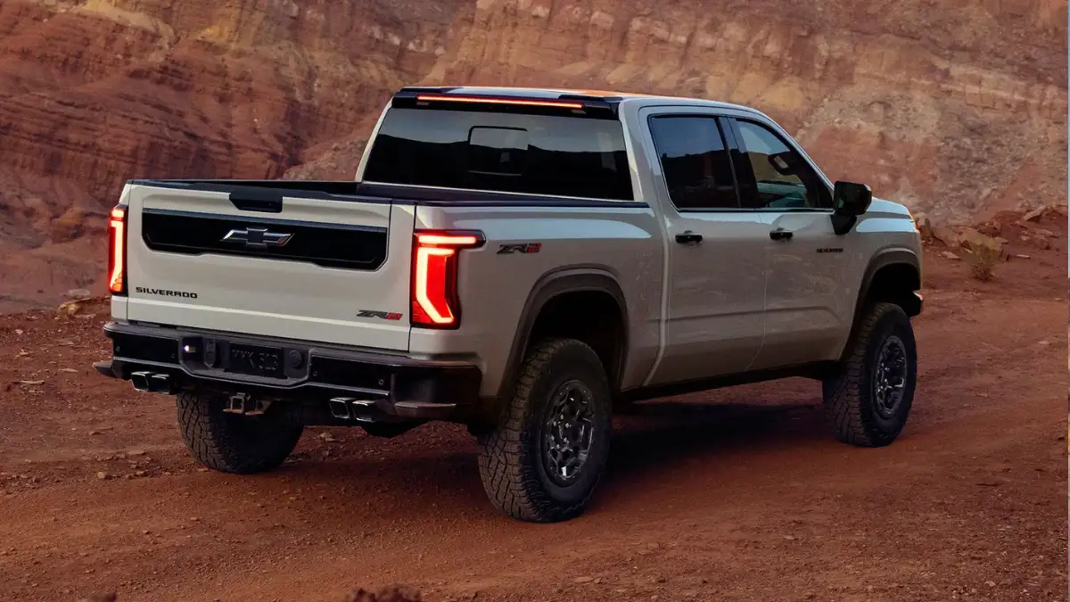A rear view of a gray Chevrolet Silverado 1500 driving on a dirt road in the desert