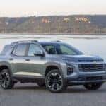Front 3/4 view of a 2025 Chevrolet Equinox LT in Sterling Gray Metallic parked near a large body of water.
