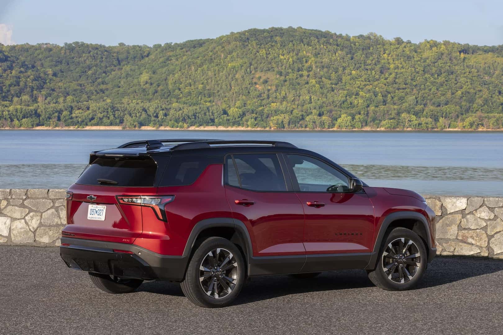 Rear 3/4 view of a 2025 Chevrolet Equinox RS in Radiant Red Tintcoat with Mosaic Black Metallic roof parked near a large body of water.