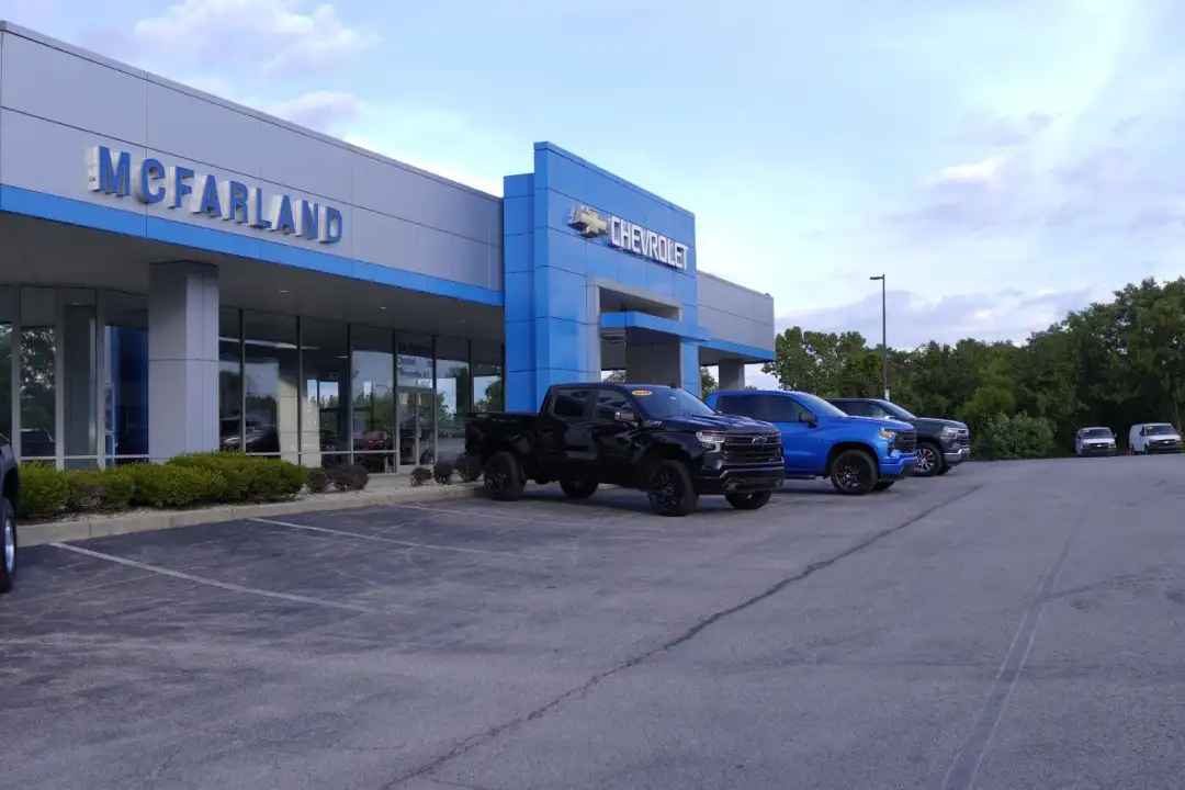 Wide exterior view of the McFarland Chevrolet dealership building in Maysville, KY, featuring a black pickup truck and a blue pickup truck parked in the front lot under a partly cloudy sky