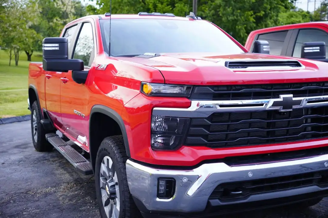 Front three-quarter view of a bright red Chevrolet Silverado 2500HD truck parked on the lot, showing its large chrome bumper, black horizontal grille, and prominent trailering mirrors