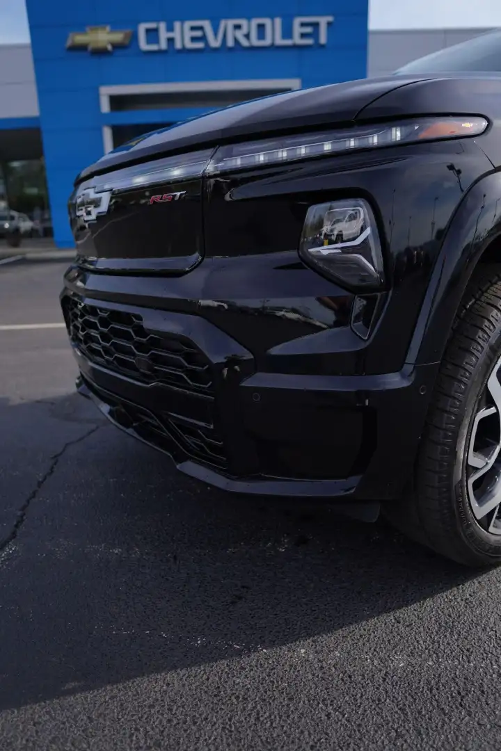 Close-up front view of a black Chevrolet Silverado EV RST electric truck parked on the dealership lot, highlighting its modern LED light bar, blacked-out grille, and RST badging