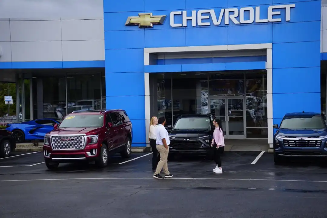 A McFarland Chevrolet dealership salesperson interacting with customers in the parking lot in front of the main showroom entrance, surrounded by a red GMC Yukon and a black Chevy SUV